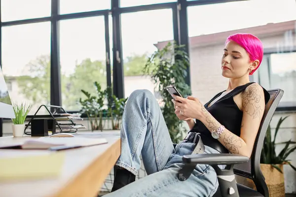 Fröhlich entspannte Arbeiterin mit Tätowierungen und rosa Haaren, die auf ihr Handy schaut, Geschäftskonzept — Stockfoto