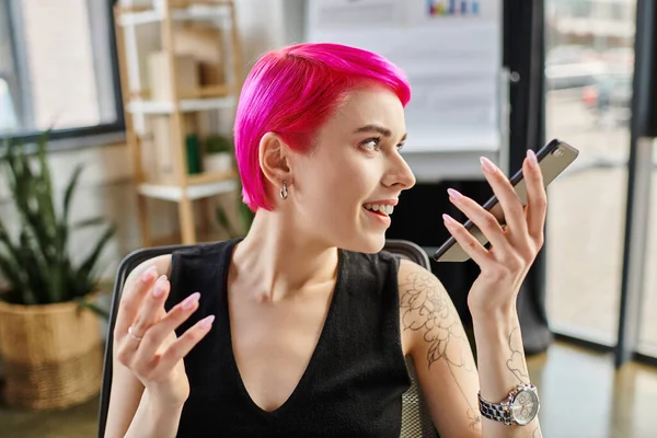 Happy pink haired female worker in casual attire talking by phone at office, business concept — Stock Photo