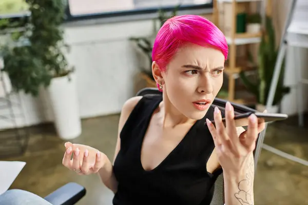 Irritated pretty businesswoman with tattoos and pink hair talking unhappily by phone at office — Stock Photo