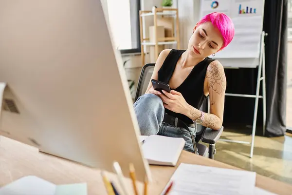 Giovane operaia dai capelli rosa con tatuaggi che guarda il suo cellulare mentre lavora in ufficio — Foto stock