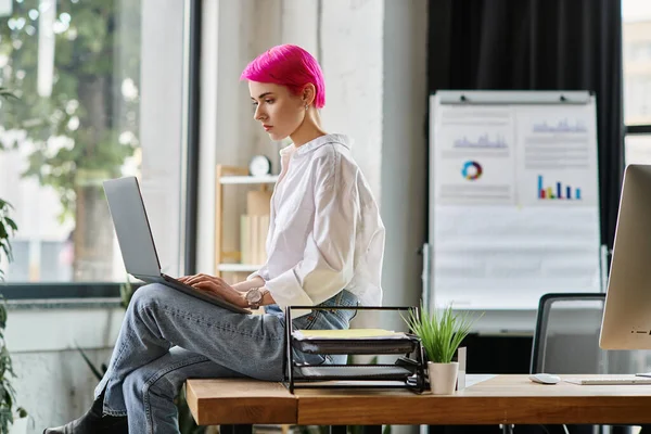 Junge attraktive Geschäftsfrau in Jeans und weißem Hemd sitzt und im Büro auf ihren Laptop schaut — Stockfoto
