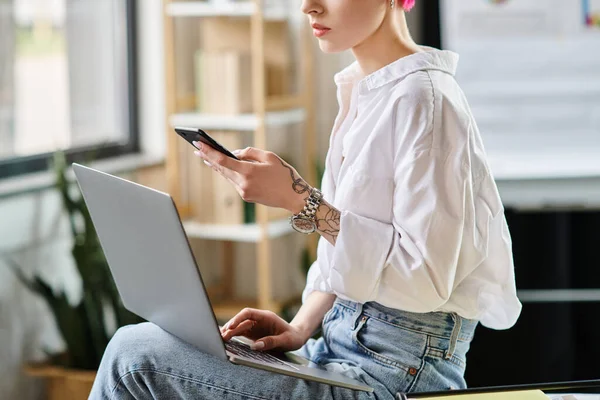 Vista recortada de la mujer de negocios en camisa blanca y jeans sentado con el ordenador portátil y mirando el teléfono - foto de stock