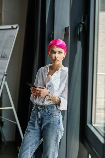 Mulher de cabelos curtos bonita em camisa branca e jeans segurando telefone celular e olhando para longe, negócio — Fotografia de Stock