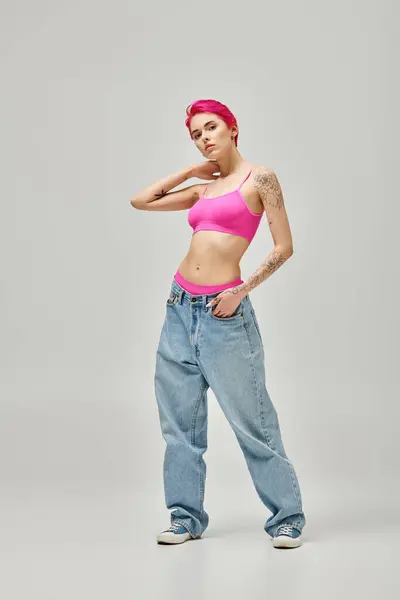 Appealing young woman with pink hair and tattoos in stylish crop top posing on grey backdrop — Stock Photo
