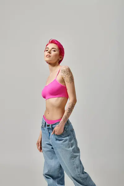 Attraente giovane donna con i capelli rosa e tatuaggio in posa con mano in tasca e guardando la fotocamera — Foto stock