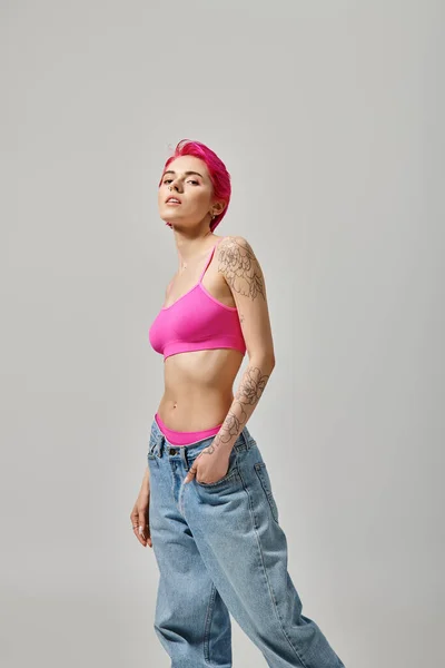 Appealing young woman with pink hair and tattoo posing with hand in pocket and looking at camera — Stock Photo