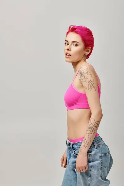Seductora mujer de pelo corto con tatuajes posando sobre fondo gris y mirando a la cámara, la moda - foto de stock
