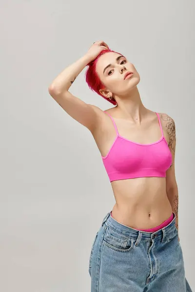 Atraente mulher de cabelos cor-de-rosa no topo da cultura e jeans posando fascinantemente em pano de fundo cinza, moda — Fotografia de Stock