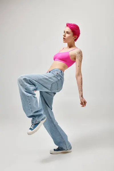 Rosa haarige Frau in stylischem Crop Top und Jeans posiert in Bewegung vor grauem Hintergrund, Modekonzept — Stock Photo