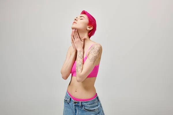 Attraktive kurzhaarige weibliche Modell in trendigen Crop Top und Jeans posiert mit den Händen in der Nähe des Gesichts — Stockfoto