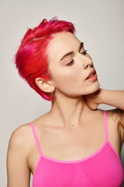 Retrato de uma jovem tatuada e perfurada com cabelo rosa olhando para o fundo cinzento — Fotografia de Stock