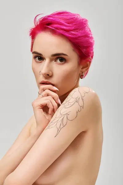 Portrait of tattooed and topless young woman with pink hair covering breasts on grey backdrop — Stock Photo