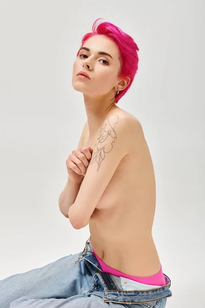 Retrato de mujer tatuada y en topless con el pelo rosa que cubre los pechos sobre fondo gris, sexy - foto de stock