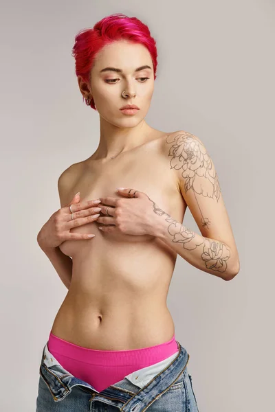 Confiança do corpo, atraente e topless jovem mulher em jeans cobrindo seios em fundo cinza — Fotografia de Stock