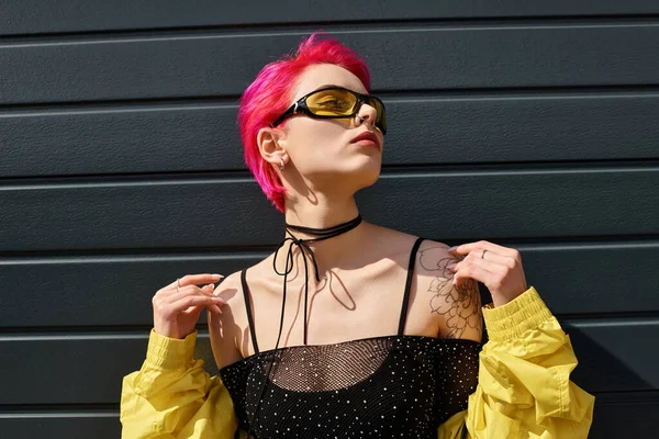 Rosafarbene junge Frau mit gelber Sonnenbrille und stylischem Outfit posiert draußen auf der Straße — Stockfoto