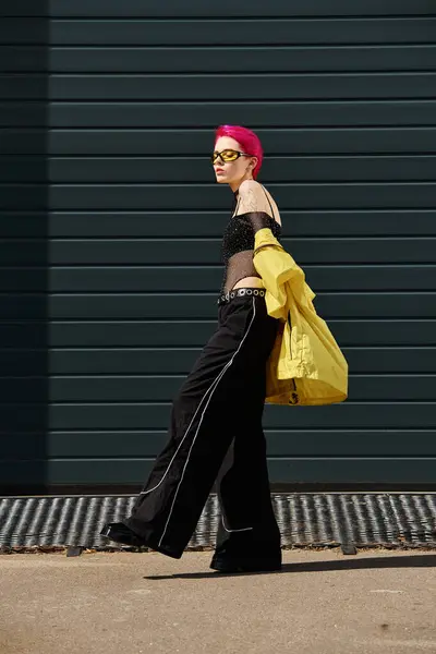 Rosa haarige junge Frau mit gelber Sonnenbrille und stylischer Kleidung, die draußen auf der Straße spaziert — Stockfoto