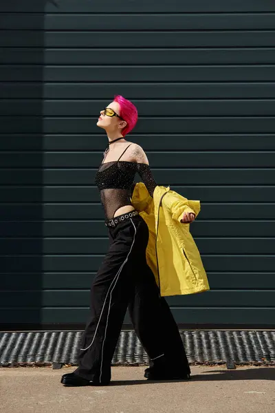 Pink haired young woman in yellow sunglasses and trendy attire walking on urban street outdoors — Stock Photo
