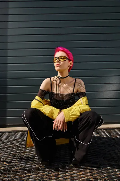 Charming woman with pink hair and tattoo posing in sunglasses and trendy streetwear on urban street — Stock Photo