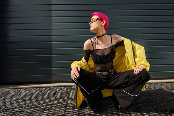 Mujer atractiva con el pelo rosa y tatuaje posando en gafas de sol y ropa de calle de moda en la calle urbana - foto de stock