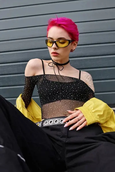 Hübsche junge Frau mit rosa Haaren und Tätowierung posiert mit Sonnenbrille und trendiger Streetwear auf der Straße — Stockfoto