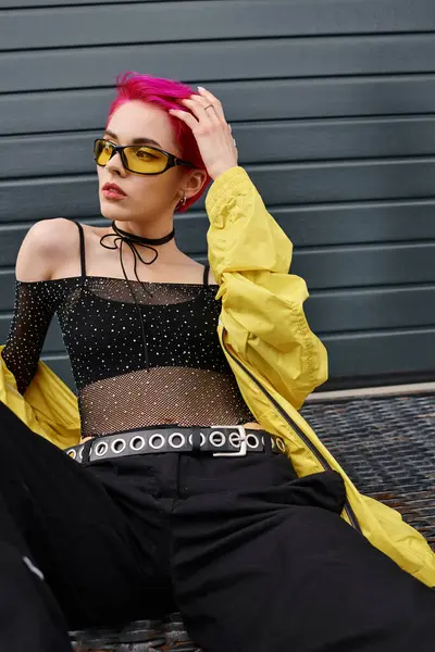 Tattooed and pink haired young woman in yellow sunglasses and trendy attire posing on urban street — Stock Photo