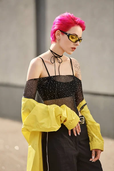 Porträt einer eleganten Frau mit rosa Haaren, gelber Sonnenbrille und trendigem Outfit, die auf der Straße posiert — Stockfoto