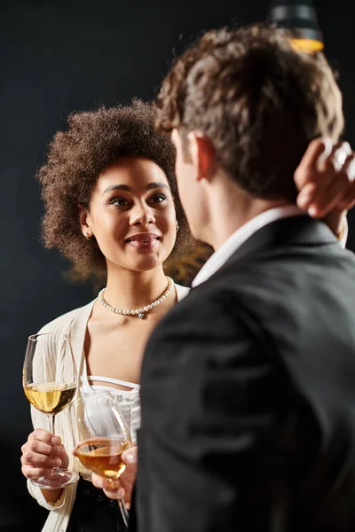 Happy african american woman holding wine glass and looking at man during date on valentines day — Stock Photo