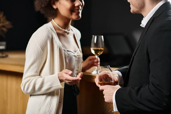 Cropped view of multicultural couple in evening attire holding glasses of wine and talking on date — Stock Photo