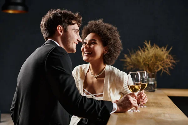 Joyful african american lady holding wine glass and looking at man during date on valentines day — Stock Photo