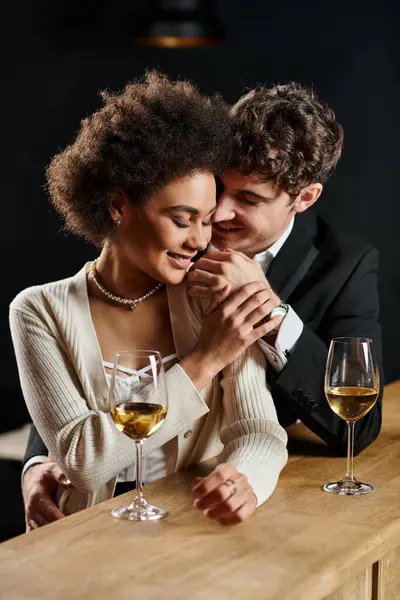 Glücklicher Mann berührt sanft die Wange einer afrikanisch-amerikanischen Frau, die mit einem Weinglas an der Theke sitzt — Stockfoto