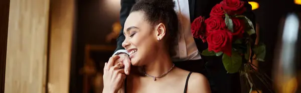 Hombre sosteniendo rosas rojas cerca de la feliz mujer afroamericana en el día de San Valentín, bandera horizontal - foto de stock