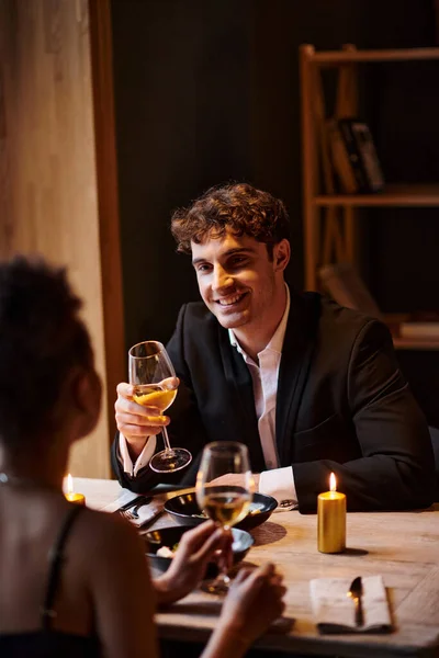 Joyful man in elegant attire looking at girlfriend with glass of wine during date in restaurant — Stock Photo