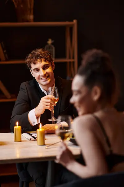 Hombre alegre en traje elegante mirando a la mujer en primer plano borrosa durante la fecha en el restaurante - foto de stock