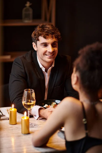 Hombre alegre en traje elegante mirando a la novia en primer plano borrosa durante la fecha en el restaurante - foto de stock