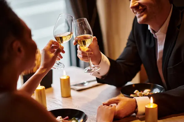 Joyful gentleman in elegant attire holding hand of girlfriend and clinking glasses during date — Stock Photo