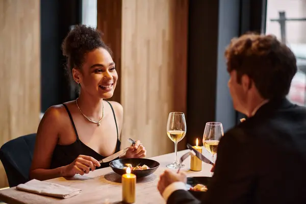 Happy african american woman enjoying meal and looking at boyfriend during date on Valentines day — Stock Photo