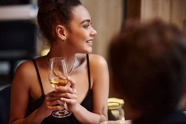 Happy african american woman smiling and holding glass of wine during date on Valentines day — Stock Photo