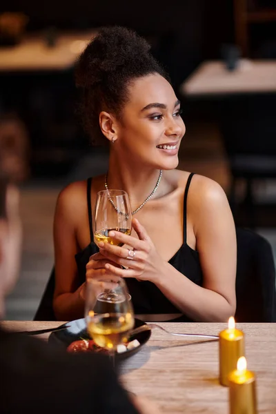 Erfreut afrikanisch-amerikanische Frau lächelt und hält ein Glas Wein beim Date am Valentinstag — Stockfoto