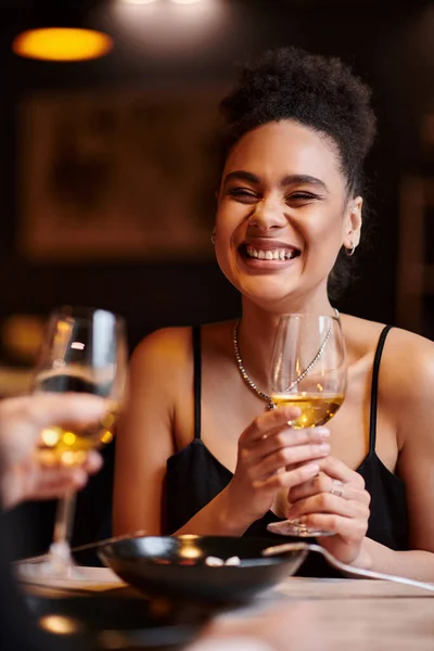 Joyful african american woman smiling and holding glass of wine during date on Valentines day — Stock Photo