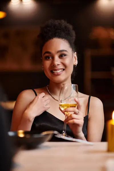Senhora americana africana alegre sorrindo e segurando copo de vinho durante a data no dia dos namorados — Fotografia de Stock