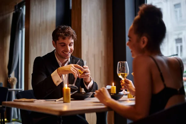 Happy man in evening attire holding glass of wine and having dinner with woman in restaurant — Stock Photo