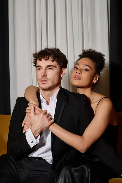 Curly african american woman in black  dress embracing good looking man in suit on velvet sofa — Stock Photo