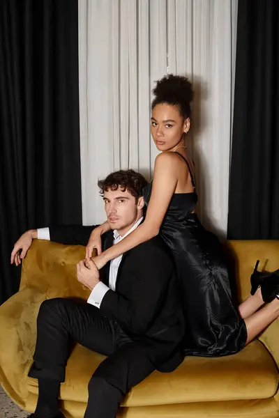 Pretty african american woman in dress embracing handsome man in suit and posing on velvet sofa — Stock Photo