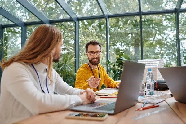 Two cheerful businessmen in casual vivid attires discussing their important startup at table — Stock Photo