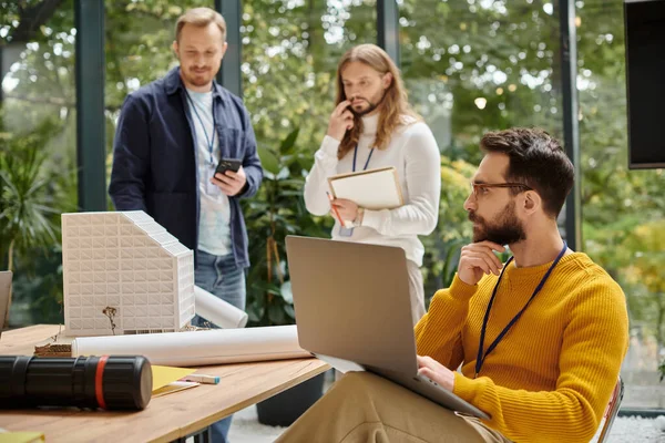 Fokus auf gutaussehenden Architekten mit Videocall, während seine verschwommenen Kollegen über Start-up diskutieren — Stockfoto