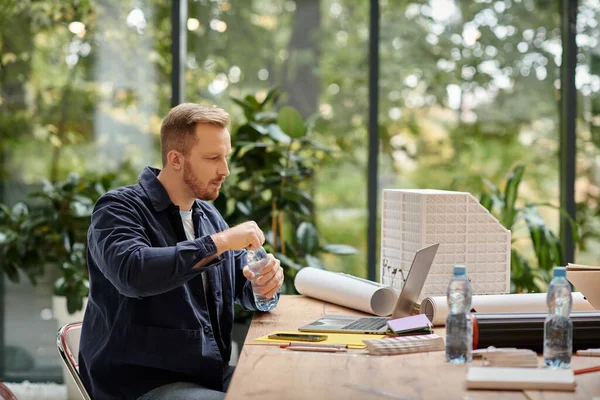 Симпатичный сосредоточенный мужчина в повседневной одежде работает над своим стартапом с ноутбуком в офисе — стоковое фото
