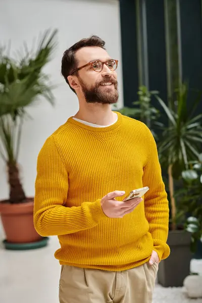 Joyous handsome architect with glasses in yellow turtleneck posing with his phone in his office — Stock Photo