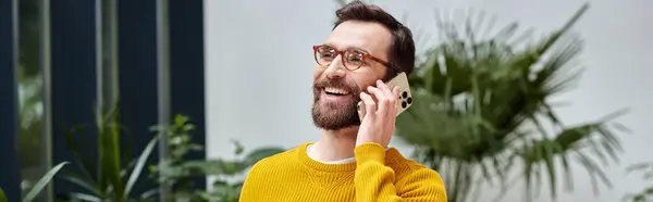 Gioioso bel architetto con occhiali in dolcevita giallo che parla al telefono nel suo ufficio — Foto stock