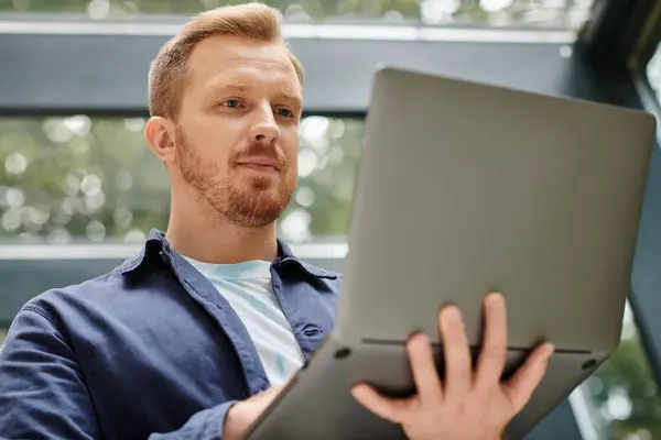 Focused good looking man in everyday comfy attire holding his laptop while working hard in office — Stock Photo