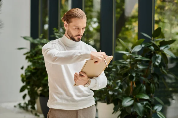 Fokussierter gutaussehender Mann in weißem bequemen Rollkragen mit Bart, der seine Papierkram beim Start-up hält — Stockfoto